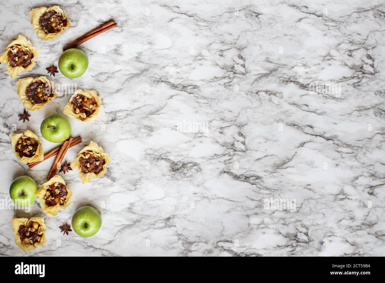 Mini tartes aux pommes avec croûte phyllo avec fruits frais, étoile d'anis et écorce de cannelle sur fond de marbre blanc et noir. Vue de dessus ou plan plat. Banque D'Images