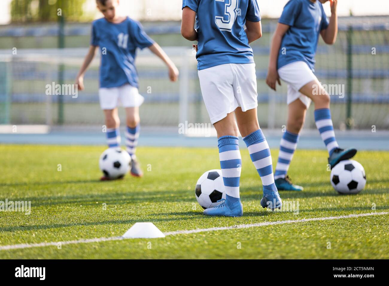 Jambes de garçons joueurs de football sur terrain d'entraînement sur gazon. Enfants en chemises bleu clair Kicking Soccer ball. Classe d'entraînement de football scolaire Banque D'Images