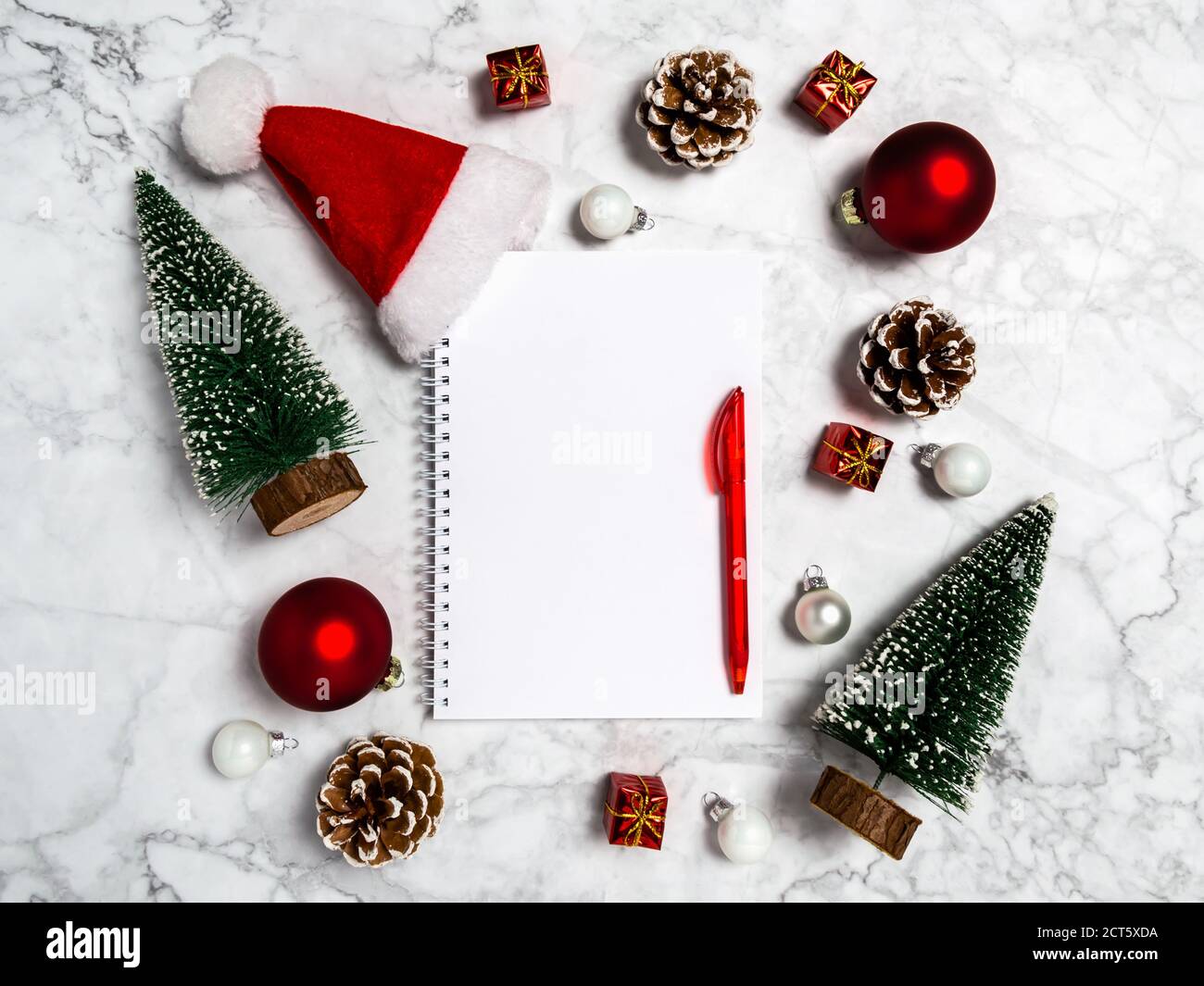 Appartement de Noël avec carnet vierge, sapins, boules, conifères, cadeaux et chapeau de Père Noël en rouge, vert, blanc sur fond de marbre. Copier l'espace pour Banque D'Images