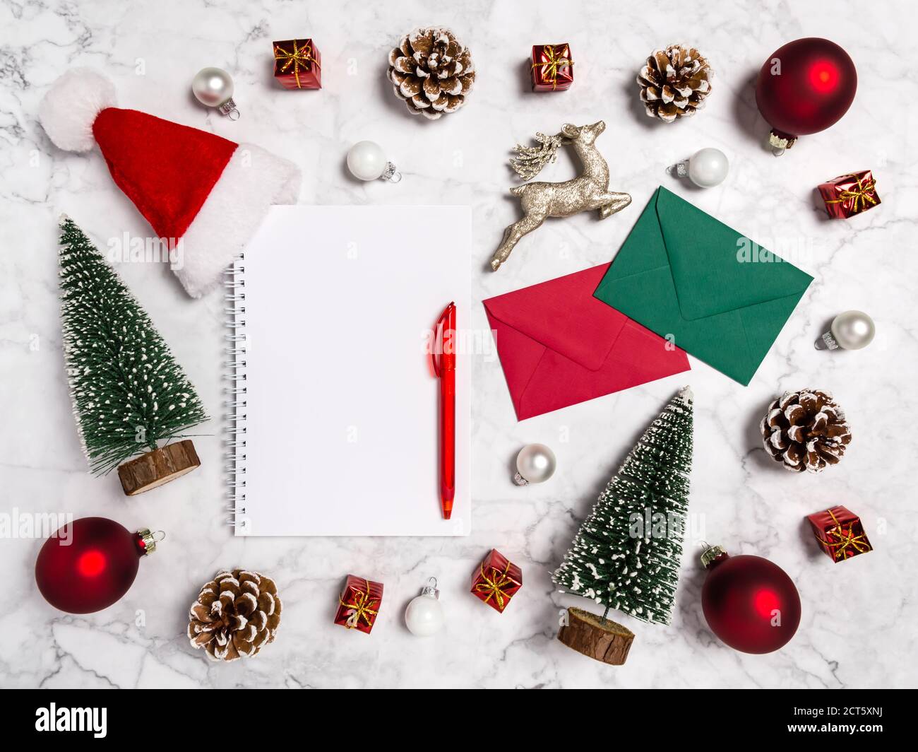 Plat de Noël avec carnet vierge, sapins, boules, conifères, cadeaux, enveloppe, renne et chapeau de Père Noël en rouge, vert, blanc sur fond de marbre Banque D'Images