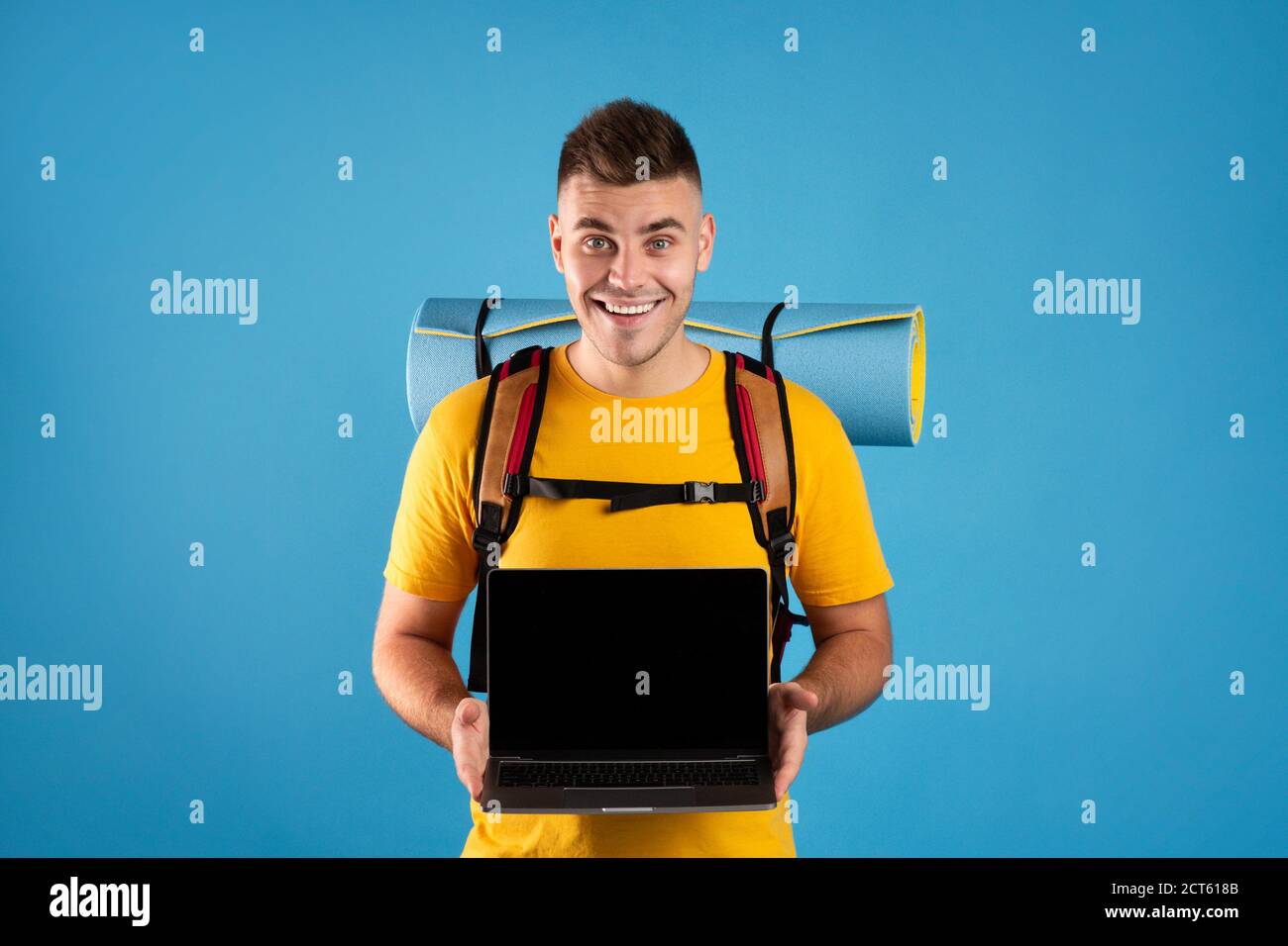 Jeune voyageur montrant un ordinateur portable avec écran vide sur fond bleu. Mockup pour le site Web de l'agence de tourisme en ligne Banque D'Images