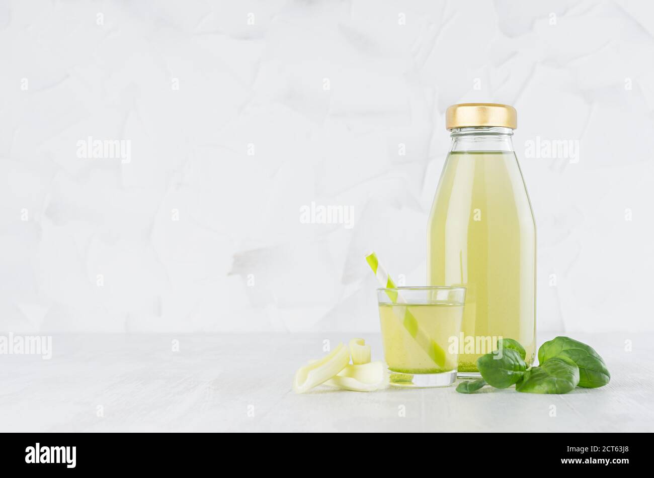 Jus de céleri et d'épinards verts frais dans une bouteille en verre, maquette avec verre, paille, tiges, feuilles dans un intérieur blanc clair et doux sur une table en bois. Banque D'Images