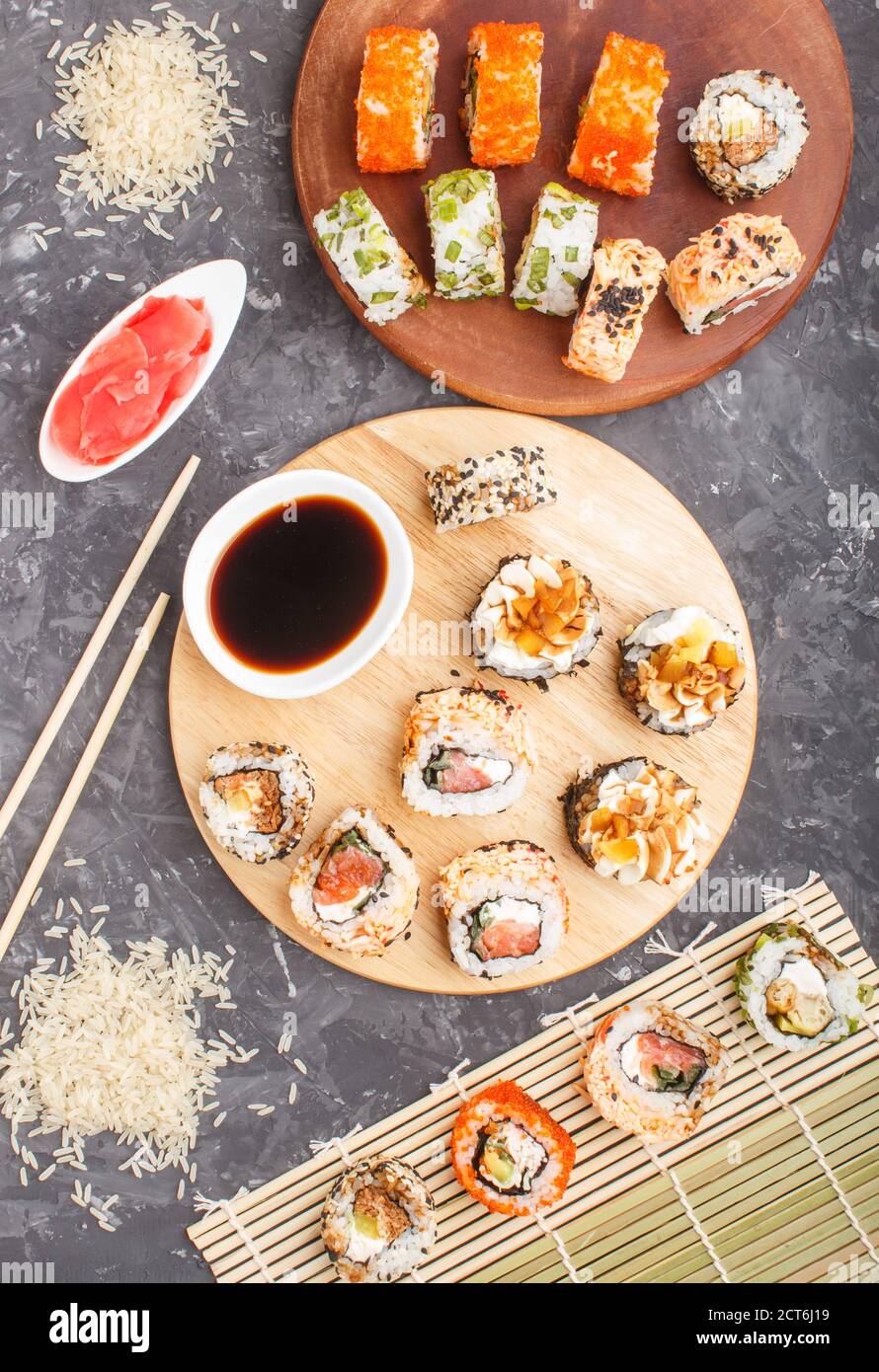 Différents types de petits pains à sushis maki avec saumon, sésame, fromage, roe et baguettes, sauce soja, gingembre mariné sur fond de béton noir. Haut v Banque D'Images