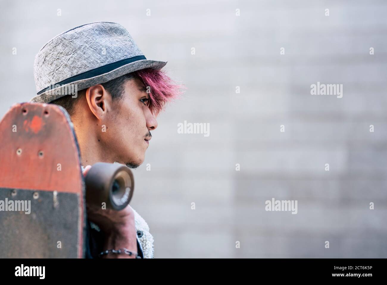 Portrait d'un jeune adolescent beau garçon regardant devant de lui et tenant un skateboard - concept de diversité et autre violet cheveux et chapeau p Banque D'Images