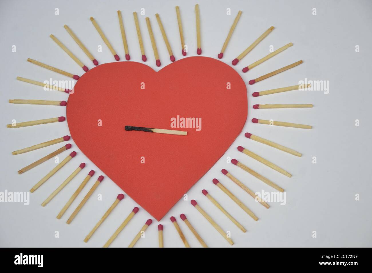 Coeur en mousse EVA rouge, avec allumettes sur le côté et un match brûlé au centre sur fond blanc, photo conceptuelle Banque D'Images