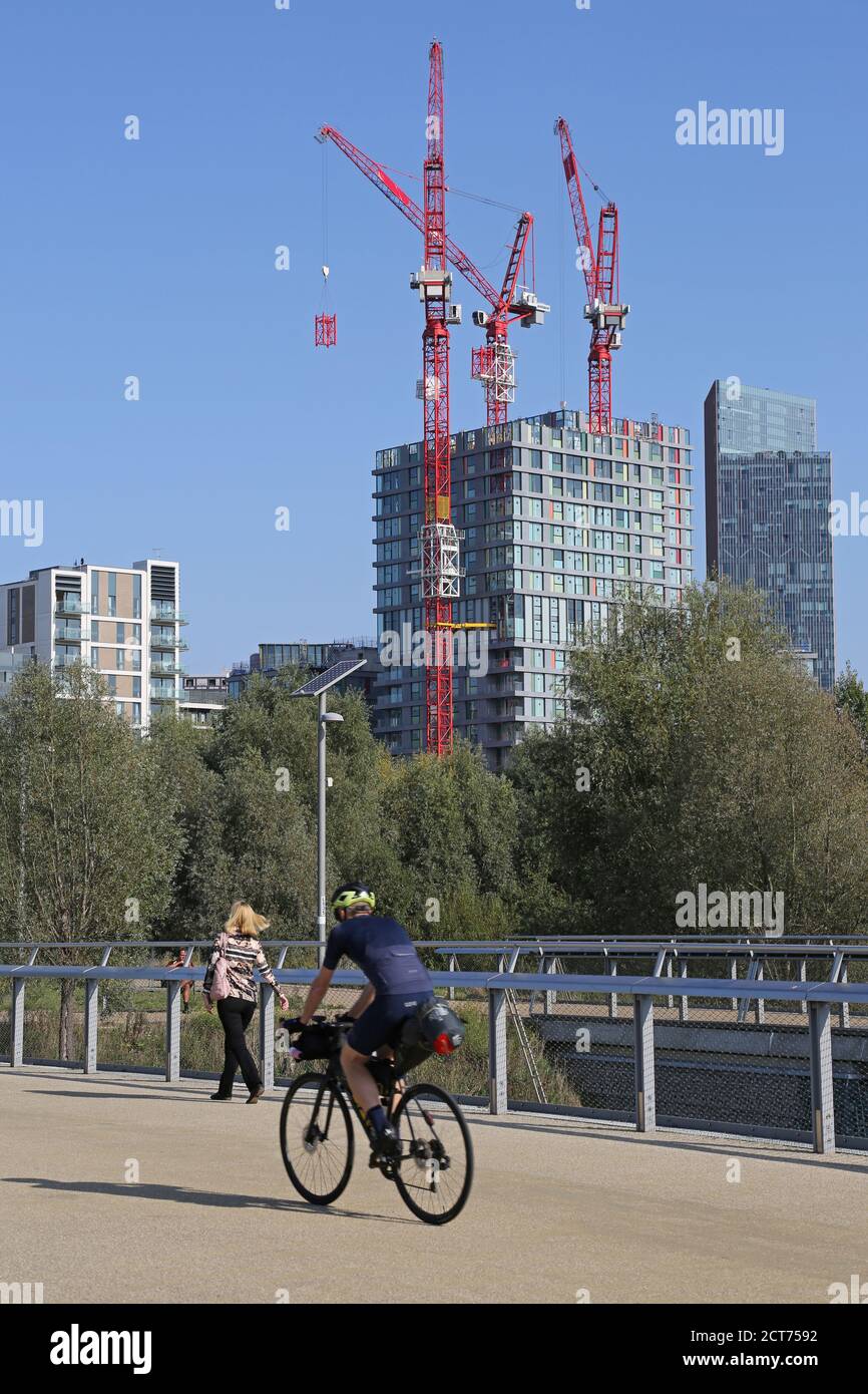 Parc olympique Queen Elizabeth, Londres. Cyclistes sur le pont East Cross. Des grues au-delà, car d'autres blocs d'appartements sont ajoutés au site du village olympique. Banque D'Images