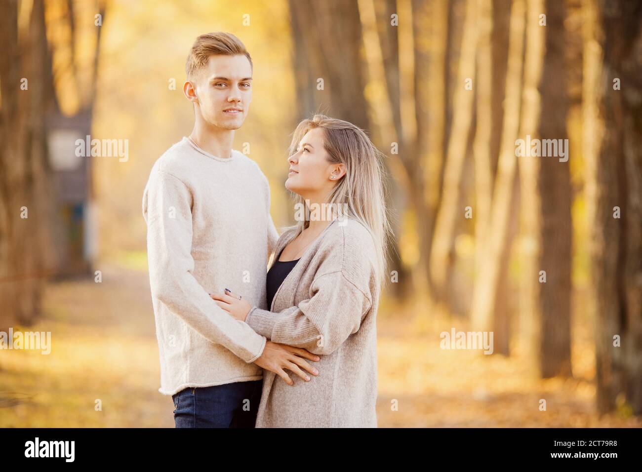 Un couple aimant s'embrasse dans la forêt d'automne dans des chandails beige clair, fond jaune avec des feuilles Banque D'Images