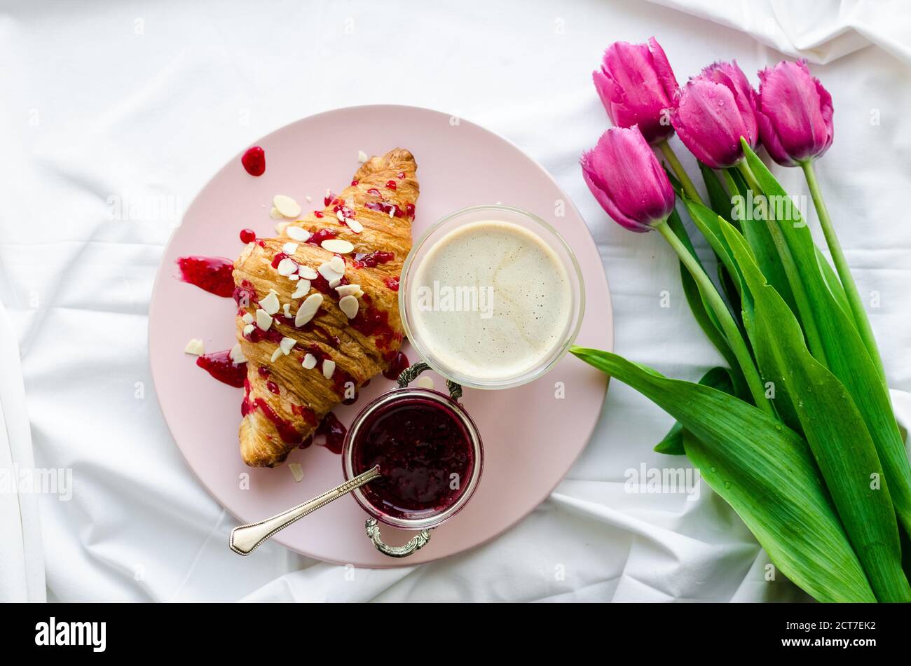 Tasse de café avec mousse et bouquet de tulipes roses sur lune de miel de lit blanc. Petit déjeuner le jour de la mère, de la Saint Valentin ou de la fête des femmes. Romantique matin co Banque D'Images