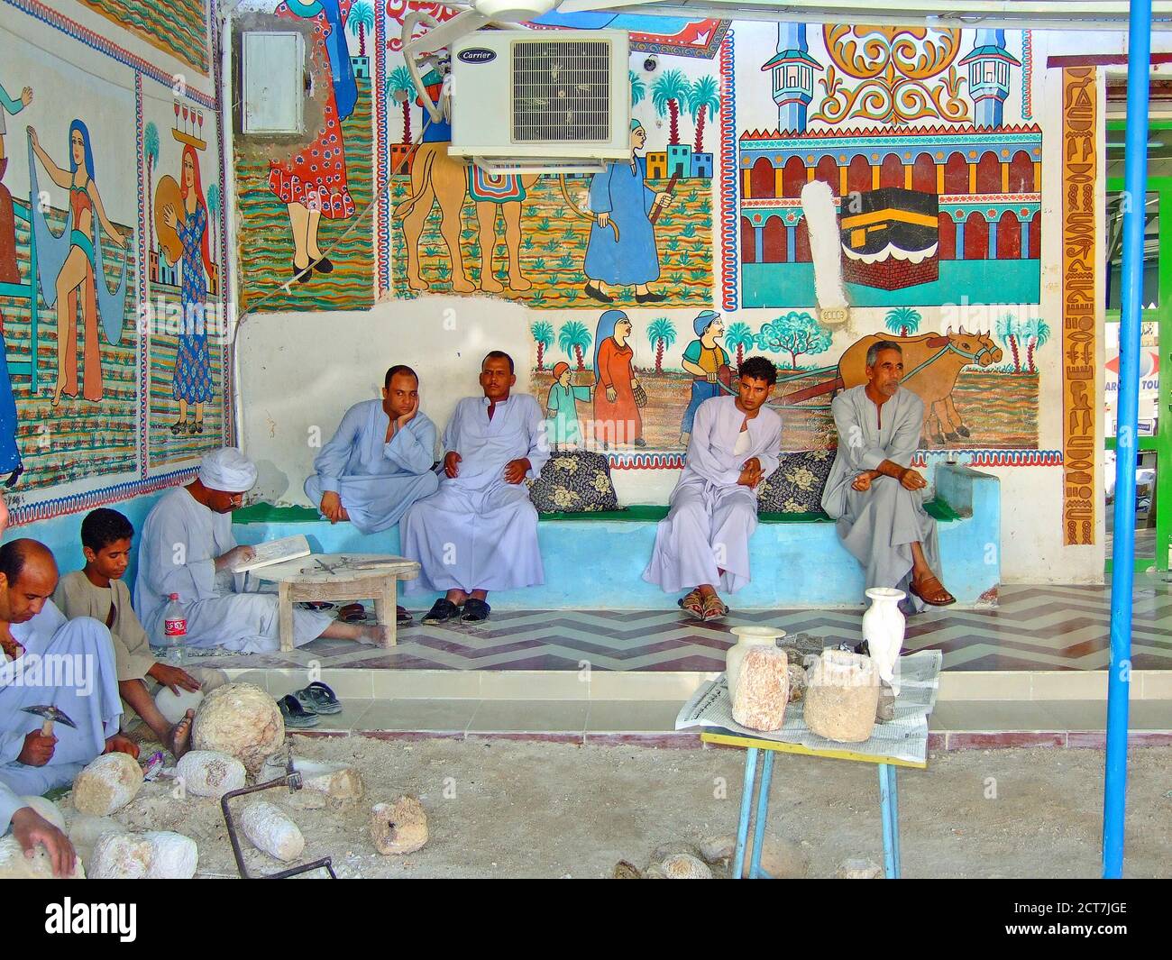 Égypte, 2013. Un groupe d'Egyptien hommes dans la robe traditionnelle de repos et de pierre sculptant contre un mur peint coloré. Banque D'Images