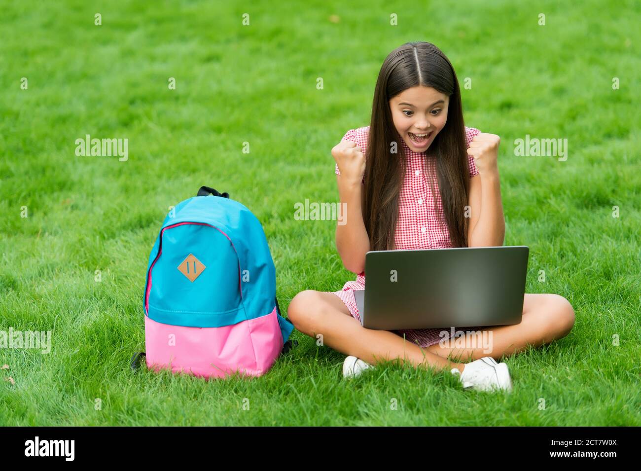 bonne fille assise sur l'herbe verte avec un ordinateur portable. Démarrage. Enfant jouant jeu d'ordinateur. Retour à l'école. Éducation en ligne. Journée de la connaissance. Cours privé d'apprentissage des enfants. Blogging. Banque D'Images