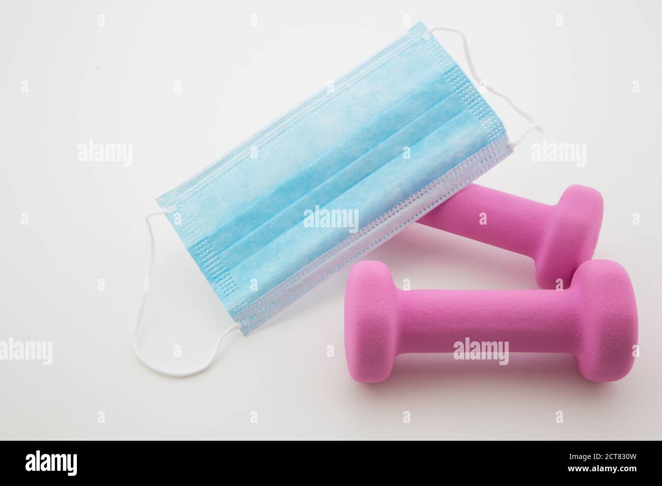Le maintien de la forme physique pendant une pandémie mondiale est difficile, comme en témoigne la situation en petits poids placés avec masque jetable contre un blanc arrière-plan Banque D'Images