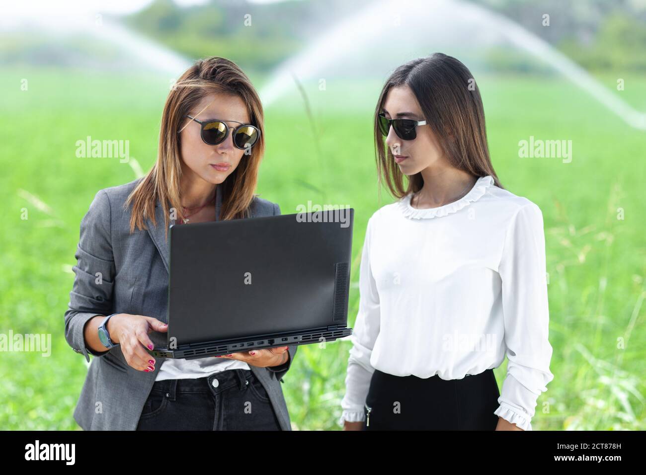 Femmes d'affaires avec un ordinateur portable dans un champ avec système d'irrigation agricole. Arroseurs d'eau en arrière-plan. Banque D'Images