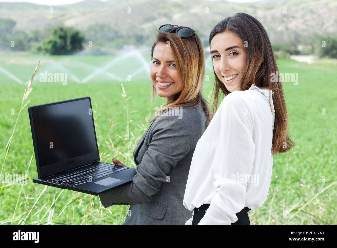 Femmes d'affaires avec un ordinateur portable dans un champ avec système d'irrigation agricole. Arroseurs d'eau en arrière-plan. Banque D'Images