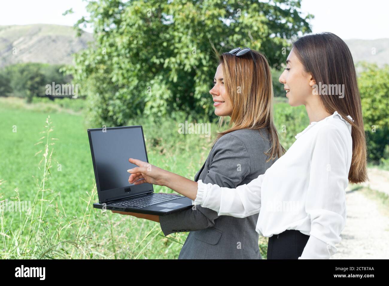 Femmes d'affaires avec un ordinateur portable dans un champ avec système d'irrigation agricole. Arroseurs d'eau en arrière-plan. Banque D'Images