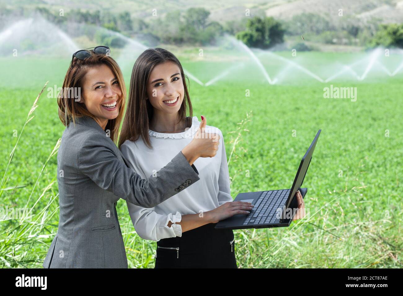 Femmes d'affaires avec un ordinateur portable dans un champ avec système d'irrigation agricole. Arroseurs d'eau en arrière-plan. Bravo. Banque D'Images