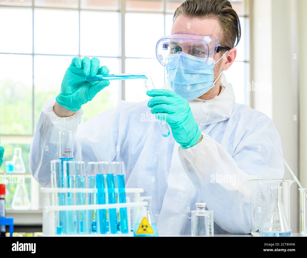 Un scientifique mâle porte une combinaison de protection pour le maintien d'un bécher ou d'un tube avec prélever du liquide à l'intérieur et travailler avec de nombreux équipements de laboratoire pour recherche en laboratoire Banque D'Images