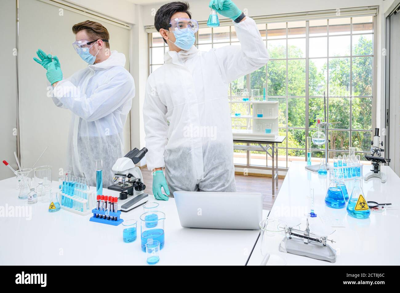 Couple de scientifiques mâles portant une combinaison de protection tenant le vaccin et travaillant avec de nombreux équipements de laboratoire pour la recherche de vaccins en laboratoire. Recherche médicale Banque D'Images