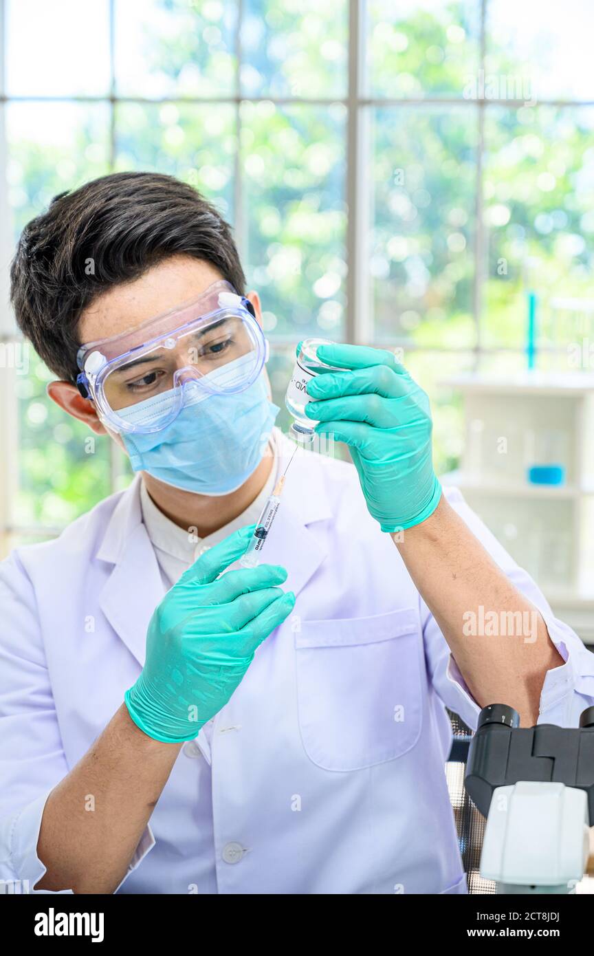 Un scientifique mâle portant une combinaison de protection contenant un vaccin contre le coronavirus et travaillant avec de nombreux équipements de laboratoire pour la recherche d'un vaccin en laboratoire. Rés. Médicale Banque D'Images