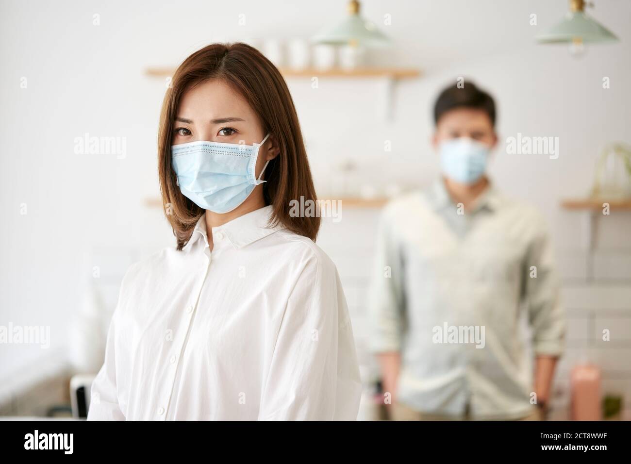 portrait d'une jeune femme asiatique portant un masque regardant appareil photo avec femme en arrière-plan Banque D'Images