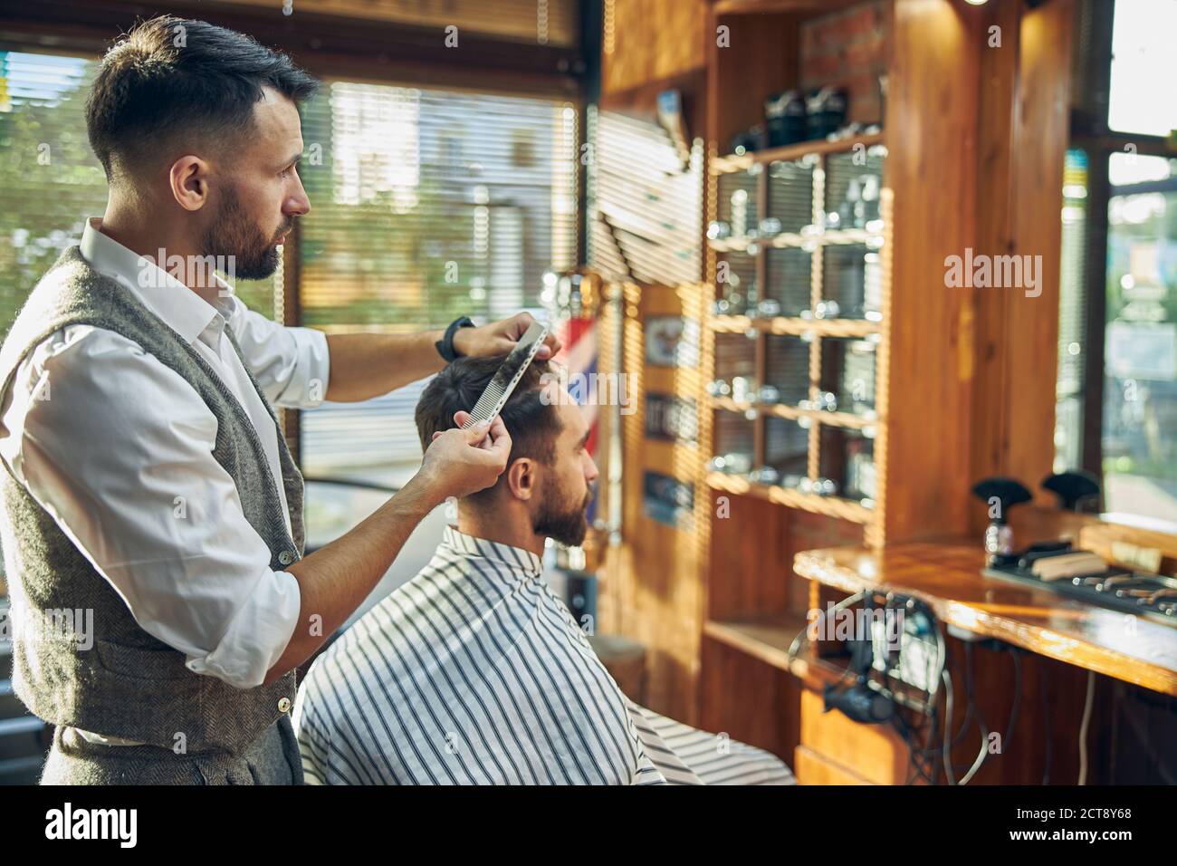 Coiffeur ambitieux travaillant sur une coupe de cheveux de son visiteur Banque D'Images