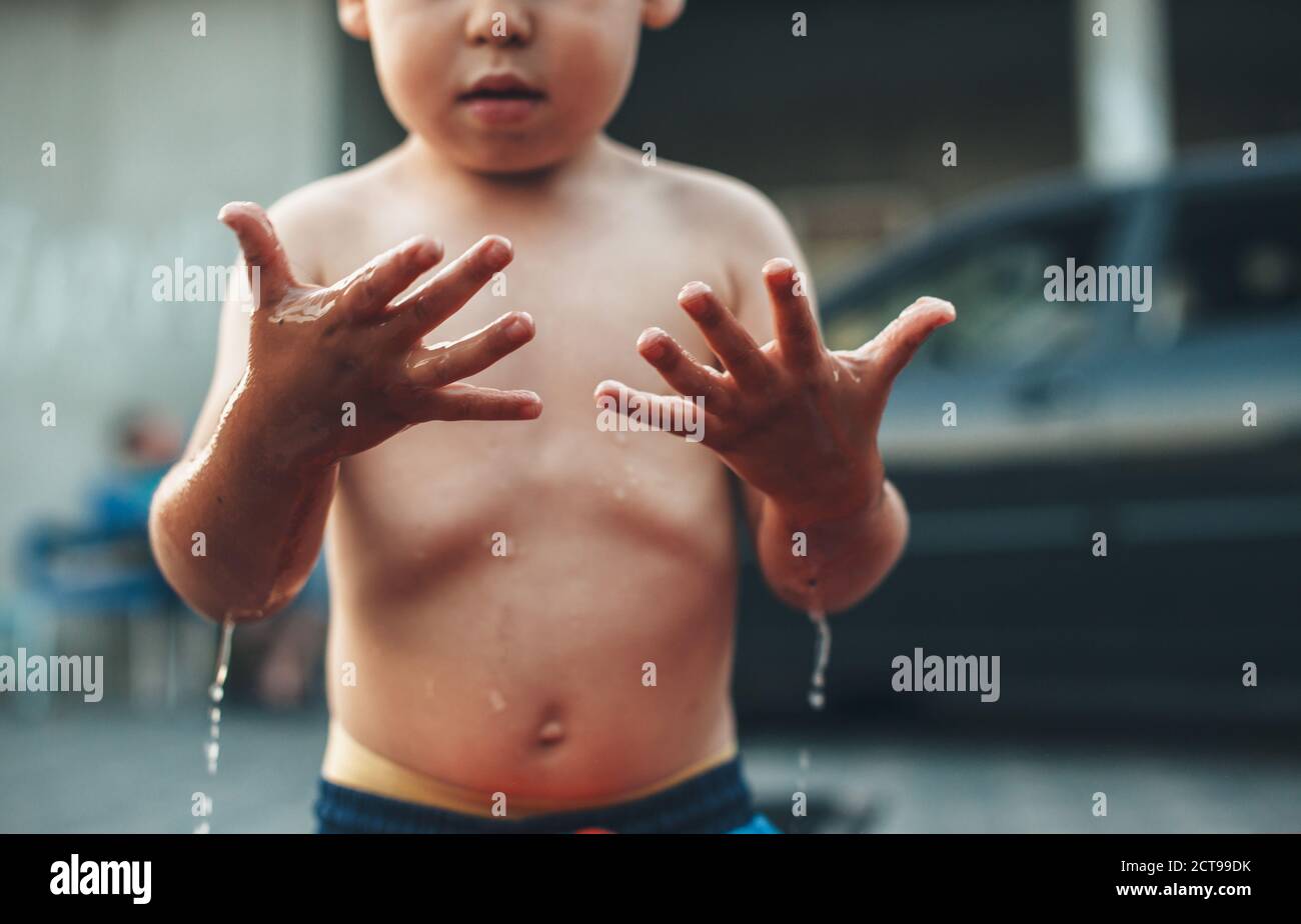 Petit enfant caucasien jouant avec de l'eau à la maison posant sans vêtements et mains mouillées Banque D'Images