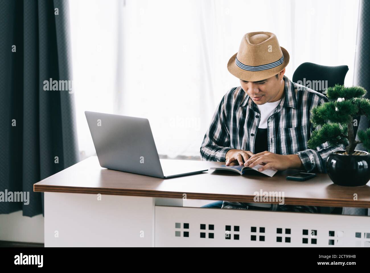 Le matin, le jeune homme asiatique heureux assis à sa table lisant au bureau à domicile, rester à la maison. Quarantaine. Banque D'Images