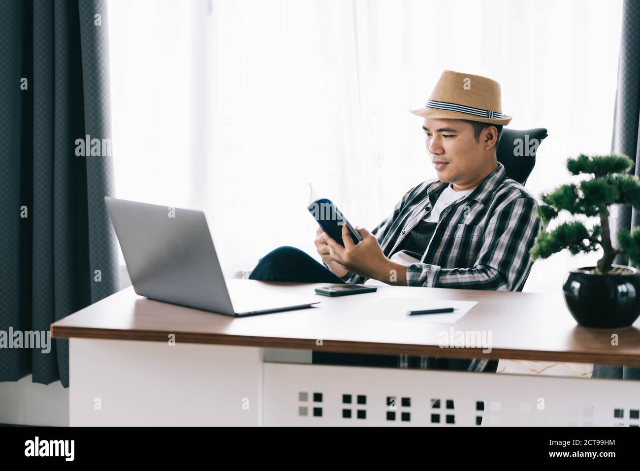 Joyeux jeune homme asiatique assis à sa table lisant au bureau à domicile, rester à la maison. Quarantaine. Banque D'Images