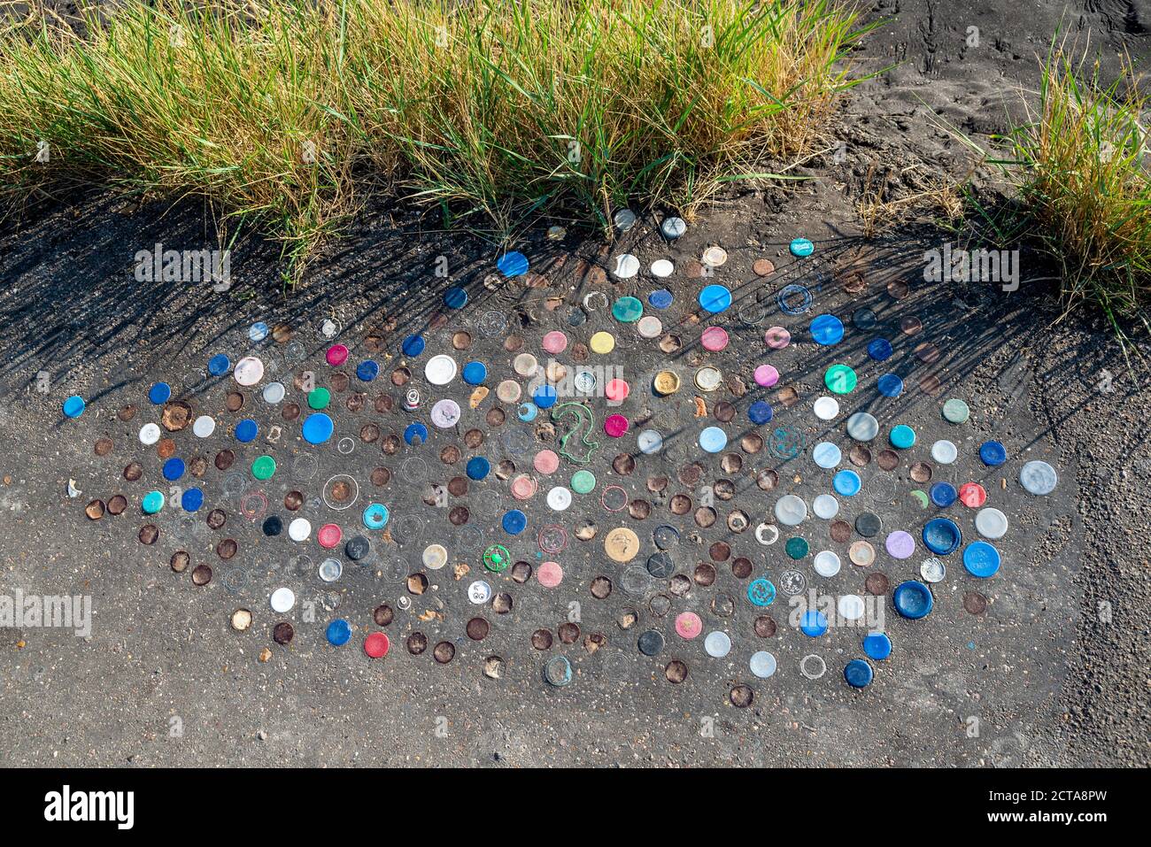 Dessus de bouteille en plastique poussé dans la couche de goudron de la digue à Chalkwell, Southend on Sea, Essex, Royaume-Uni. Chemin de cendre sur l'estuaire de la Tamise avec bouchons de bouteille Banque D'Images