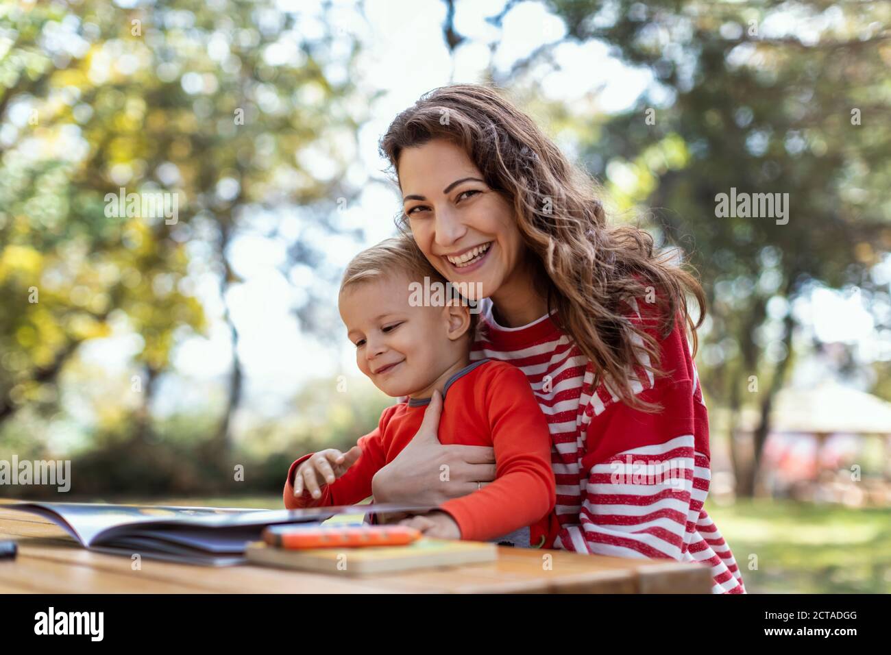 Livres de lecture de mère et de fils au jardin, avec des crayons sur la table de pique-nique, mère regardant la caméra Banque D'Images