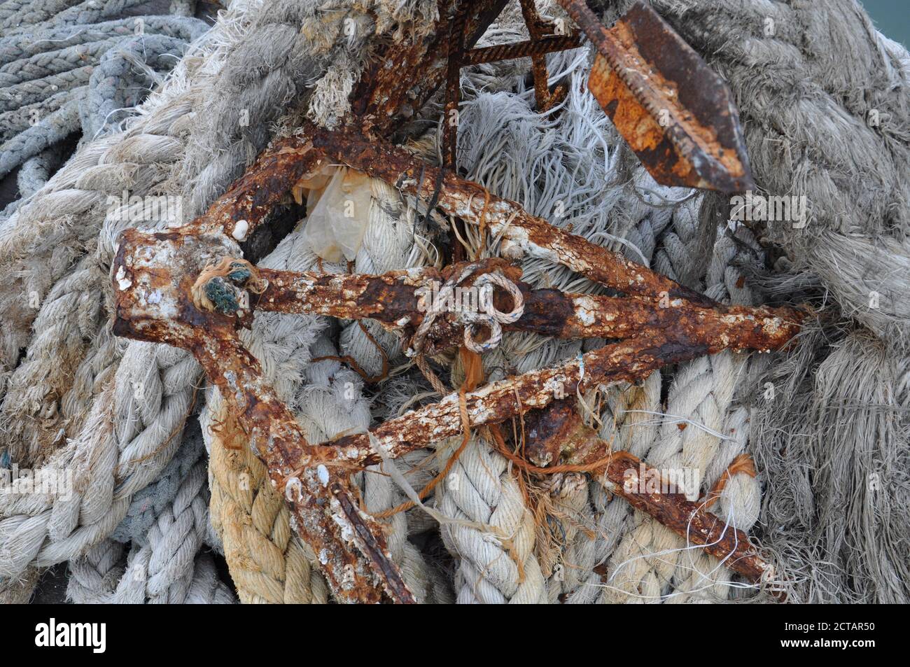 Vue aérienne d'une ancre métallique rouillée et couverte de barnacle, située sur une pile de cordes de jute épaisses. Banque D'Images