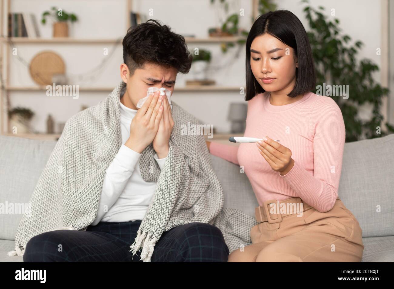 Petite amie qui traite un Boyfriend malade qui donne un médicament assis sur un canapé à l'intérieur Banque D'Images