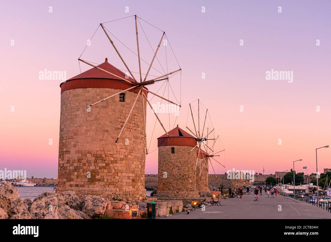 Coucher de soleil sur l'île grecque au-dessus des moulins à vent bordant le port de Mandraki, ville de Rhodes, île de Rhodes, Grèce Banque D'Images