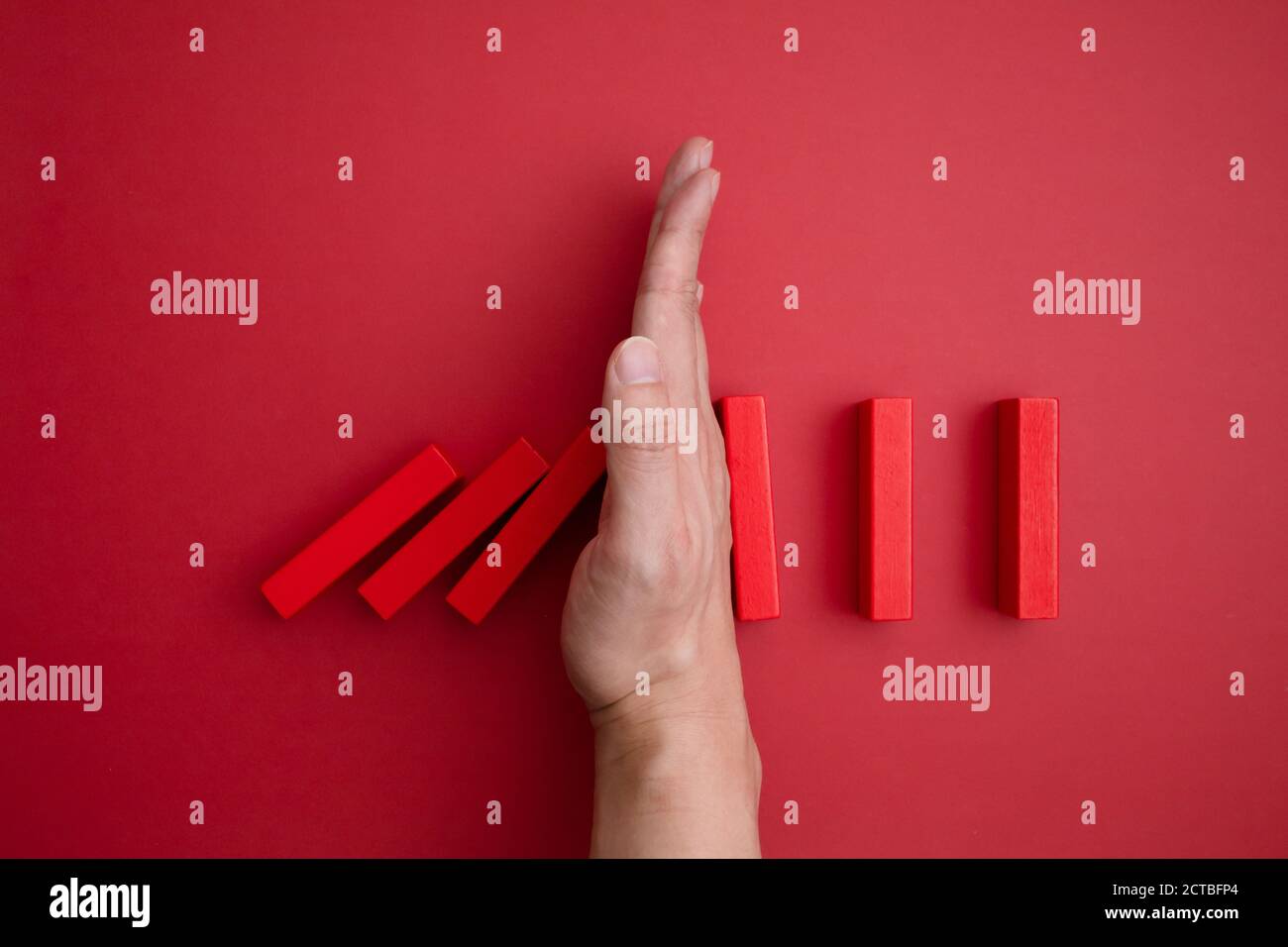 red domino blocs qui commence à tomber et une main qui l'empêche de tomber. Banque D'Images