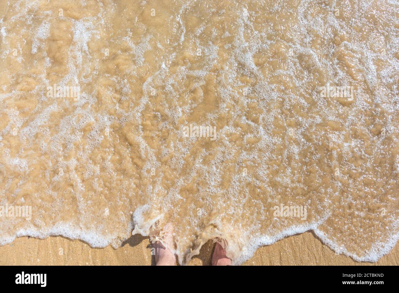 L'homme tient des pieds dans le surf d'une plage de sable Banque D'Images