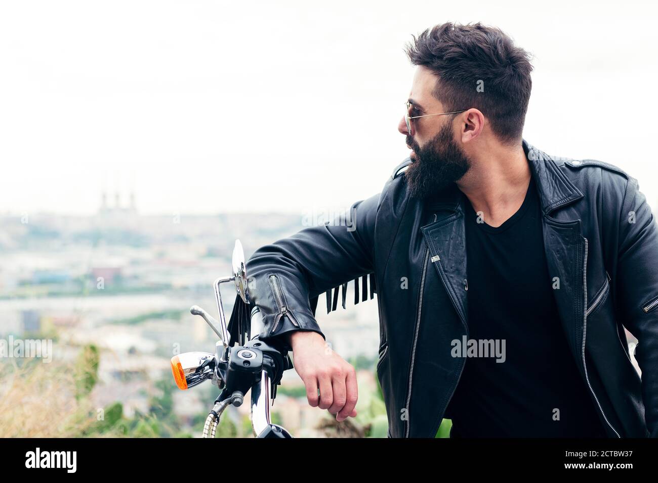 portrait d'un homme barbu dans une veste en cuir adossée au guidon de sa moto, concept de liberté et de style de vie de motard, espace de copie pour Banque D'Images