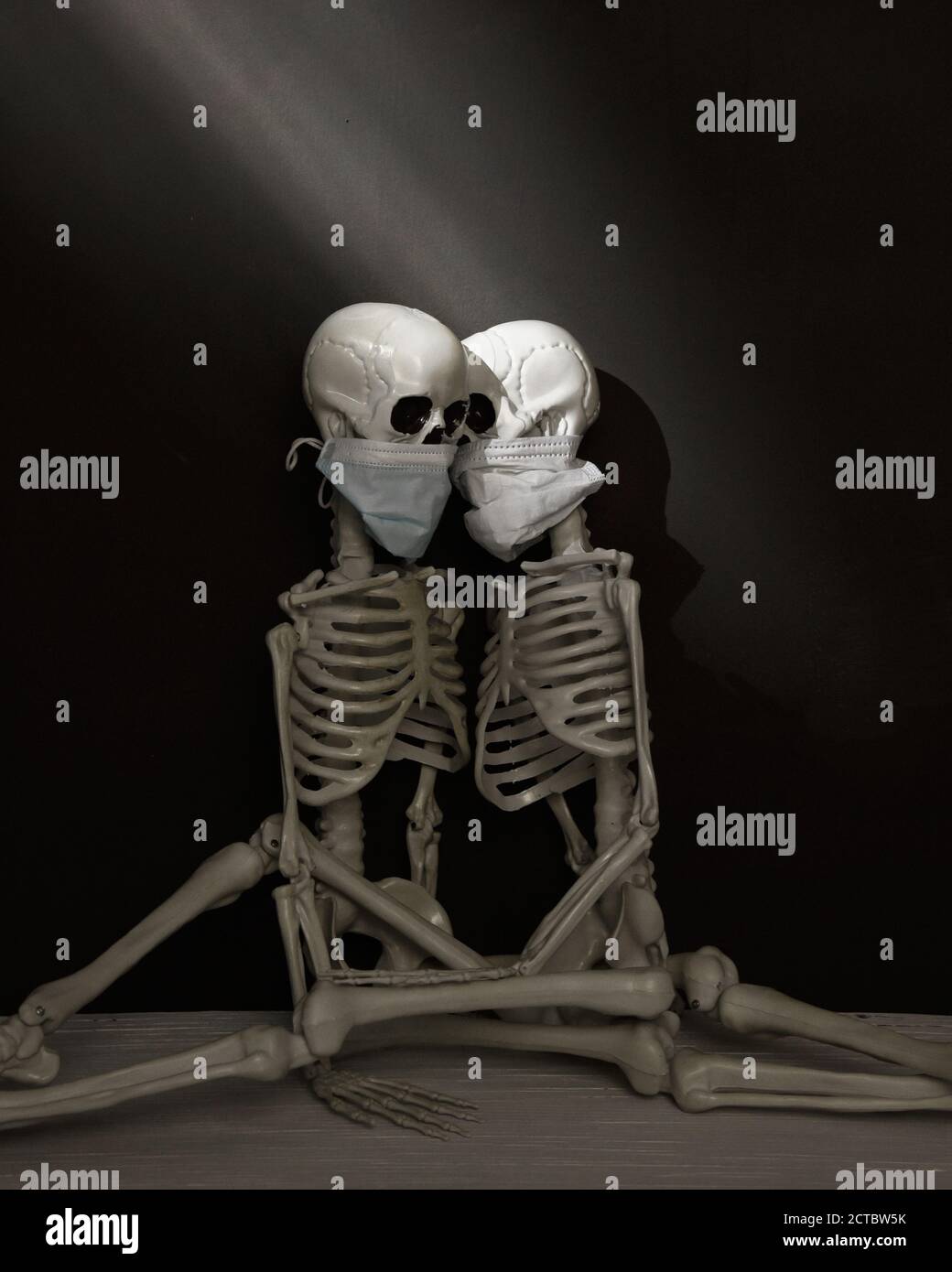 Deux squelettes humains sont assis ensemble dans une pièce sombre portant des masques pour un étrange concept de santé du virus pandémique. Banque D'Images
