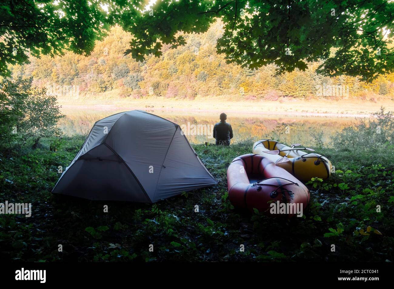 Homme près de la tente et des rabots dans le camp forestier près de la rivière. Packrafting. Concept de vie active Banque D'Images