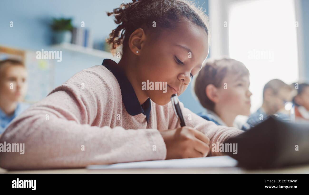 Dans l'école primaire, la classe Noire écrit dans le cahier d'exercices, passer le test. Salle de classe junior avec divers groupes d'enfants lumineux travaillant Banque D'Images