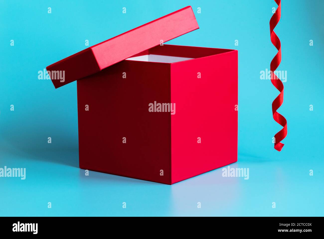 Boîte cadeau rouge avec couvercle entrouvert et ruban en spirale sur fond bleu clair. Gros plan. Concept de vacances. Maquette de message d'accueil ou de publicité Banque D'Images