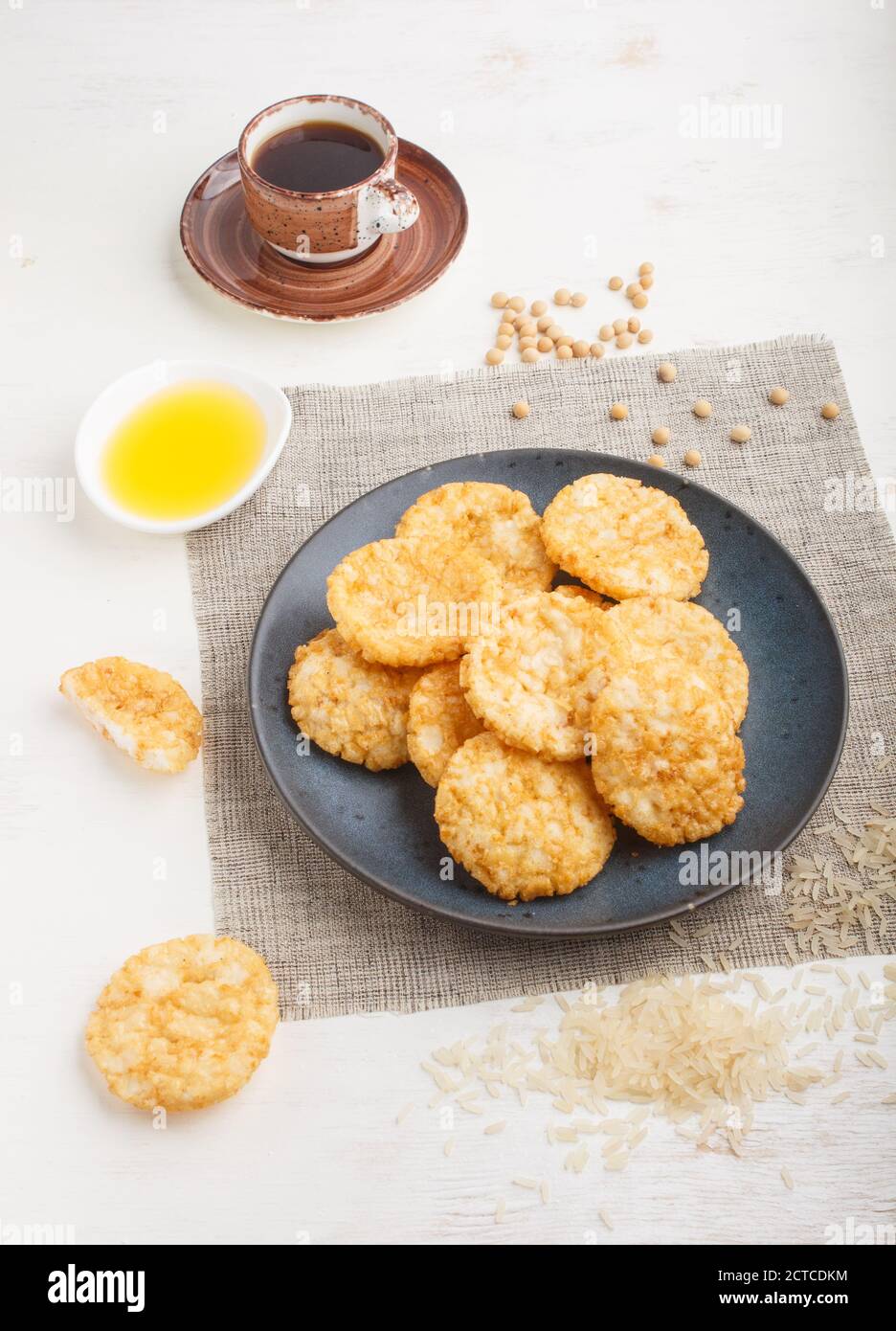 Biscuits japonais traditionnels aux chips de riz avec sauce au miel et au soja sur une assiette en céramique bleue et une tasse de café sur fond de bois blanc. Vue latérale, Banque D'Images