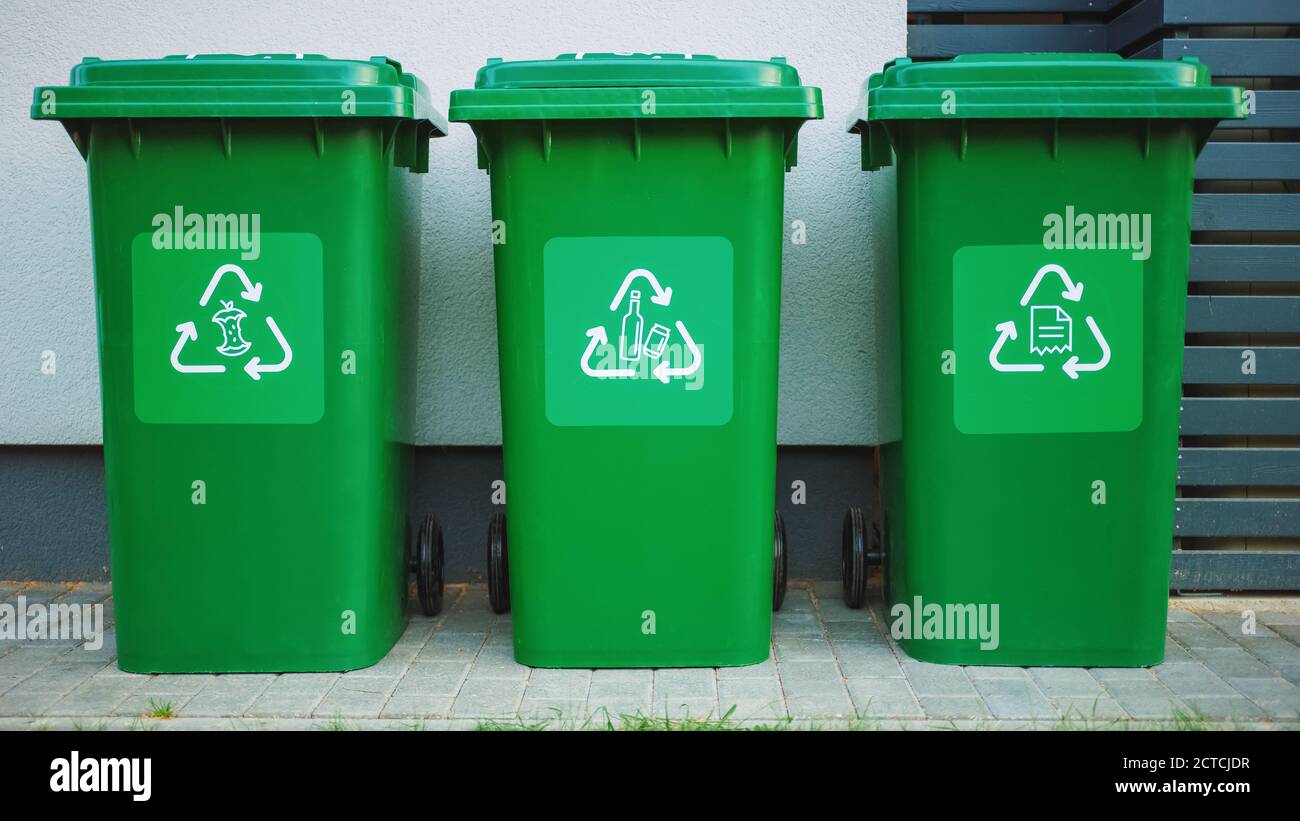 Poubelles en plastique de couleur verte, avec différents logos de recyclage à l'avant, empilées en rangée contre un mur en bois brun. Concept de tri des déchets alimentaires Banque D'Images