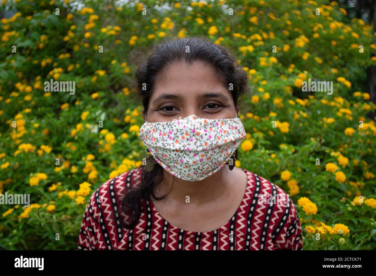 Belle dame avec masque floral, boucles d'oreilles et supports haut de gamme de designer avant les fleurs jaunes. Protection contre le corona avec élégance. Banque D'Images