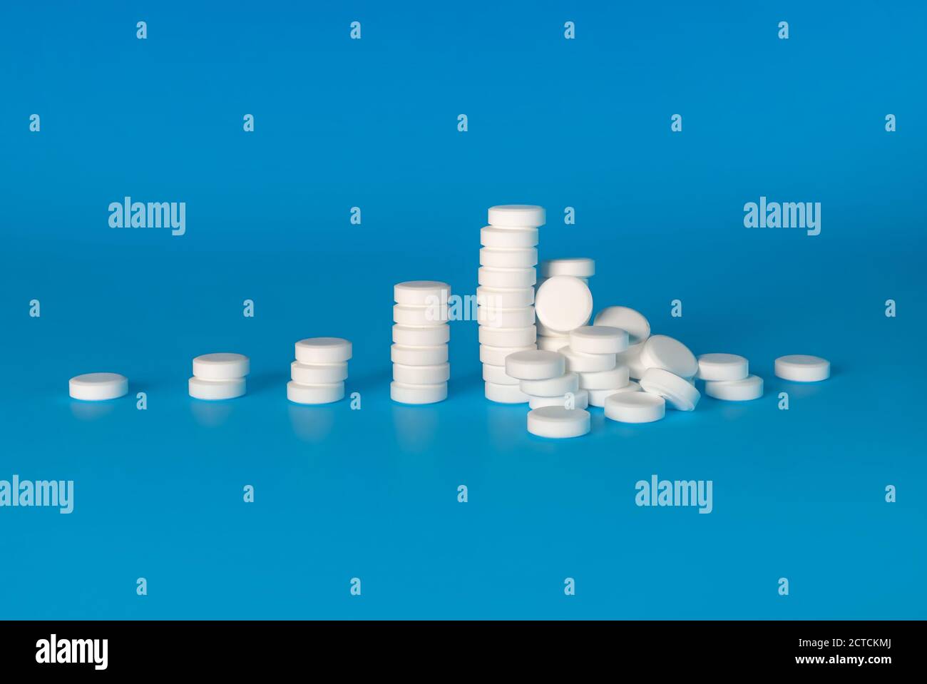 Notion d'escalade de la consommation de drogues, d'abus de substances ou de toxicomanie. Les piles de pilules blanches se développent de gauche à droite, se terminant par une pile de pilules tombées. Banque D'Images