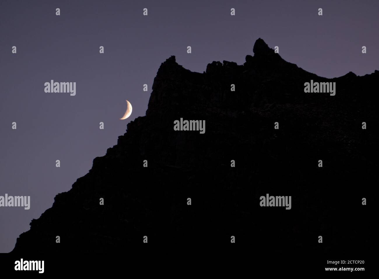 Lune en croissant avec silhouette de crête de montagne contre ciel clair la nuit Banque D'Images