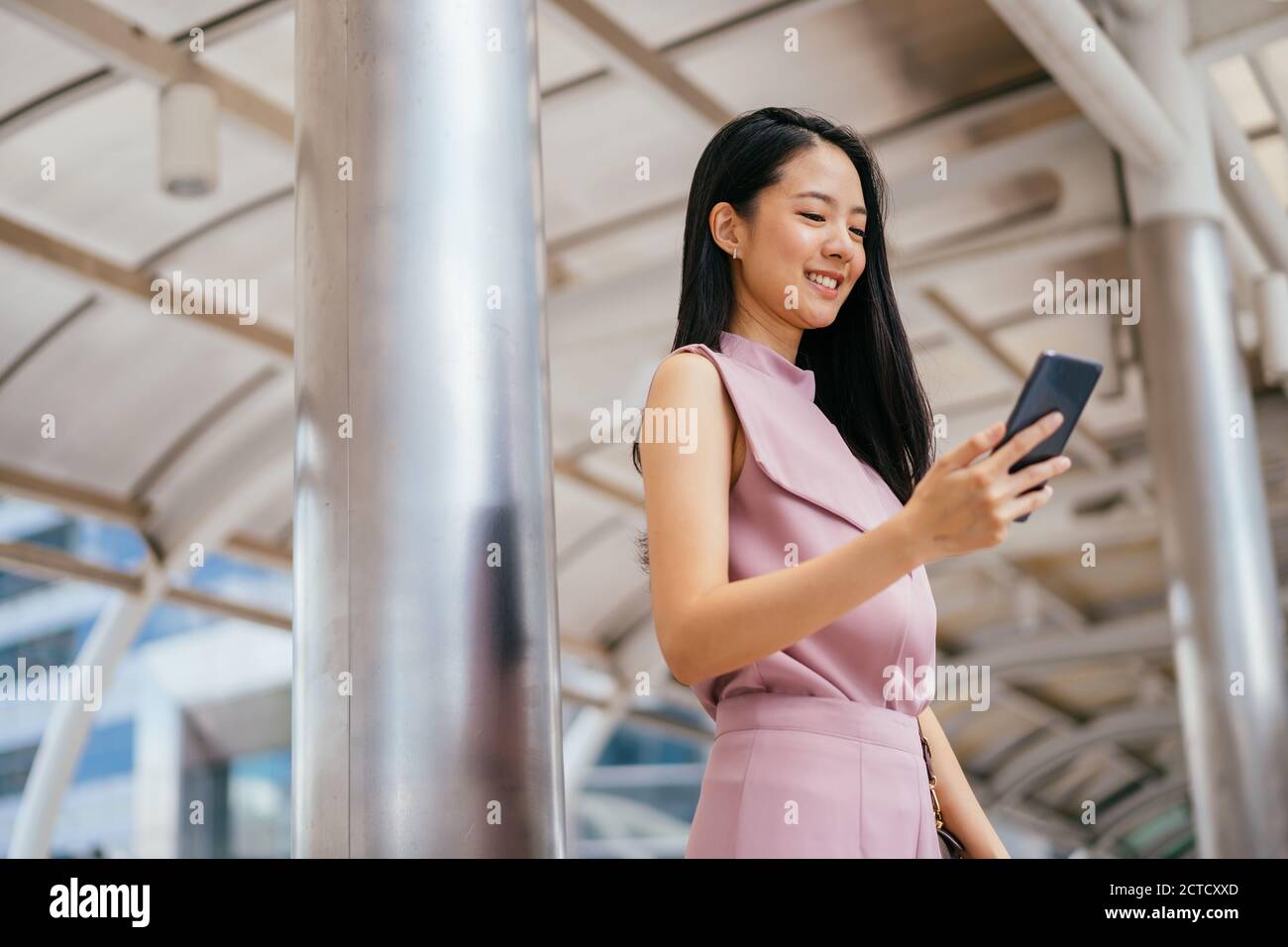 Femme d'affaires avec de longs messages de cheveux noirs sur smartphone, en déplacement, affaires, connectivité, bonheur Banque D'Images