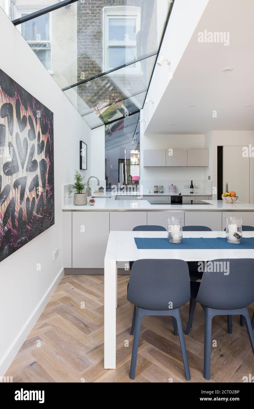 Cuisine moderne avec parquet, cuisine blanche et table à manger avec chaises bleues. Banque D'Images