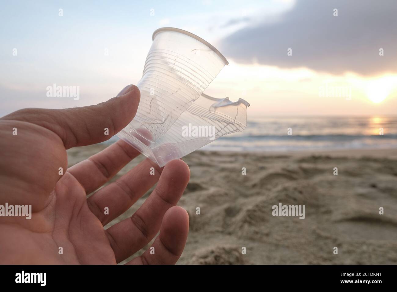 Homme main gros plan avec verre plastique isposable jeté sur sable côte de mer, pollution Banque D'Images