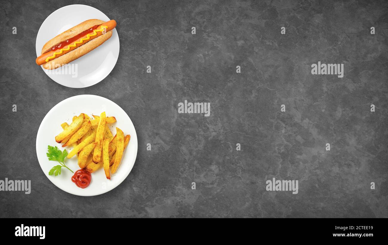 Vue de dessus des fast-foods. Hot dog et frites isolées sur un fond sombre avec espace de copie. Aliments malsains. Composition des aliments. Banque D'Images