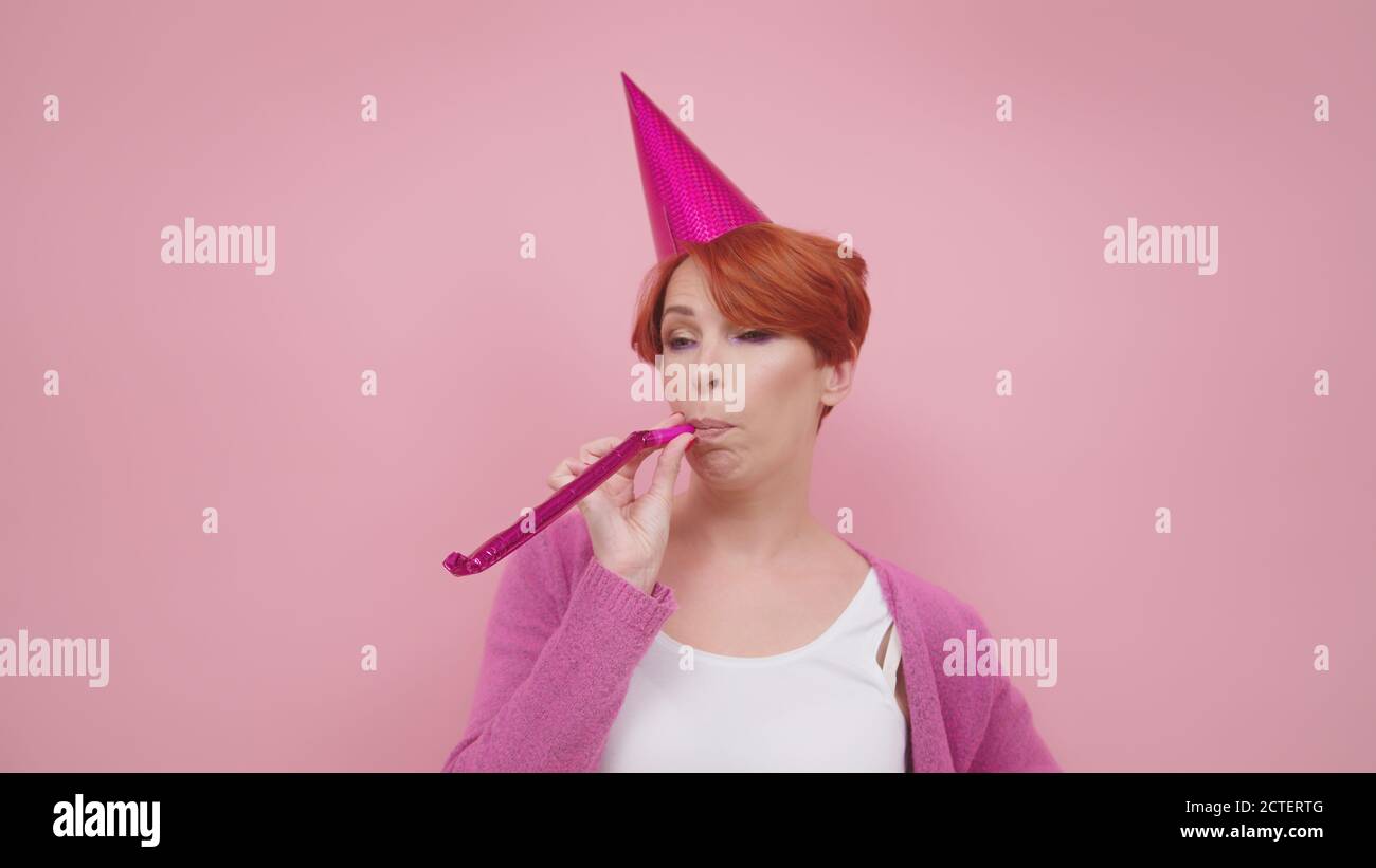 Femme d'âge moyen aux cheveux rouges lassés qui soufflait de corne sur la fête d'anniversaire. Couleurs violettes. Photo de haute qualité Banque D'Images
