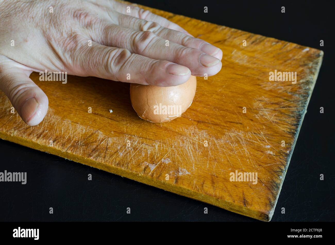 Une main mâle tient un œuf de poulet bouilli dans sa coquille contre la planche à découper. Méthode de nettoyage des coquilles. Cuisson. Mise au point sélective. Banque D'Images